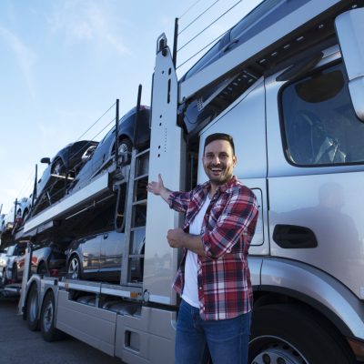 Middle aged trucker in front of truck trailer with cars.